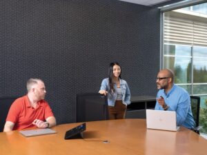 One female and two males in medium conference room with an HP Slice Microsoft Teams Rooms touch display and two HP laptops in view.