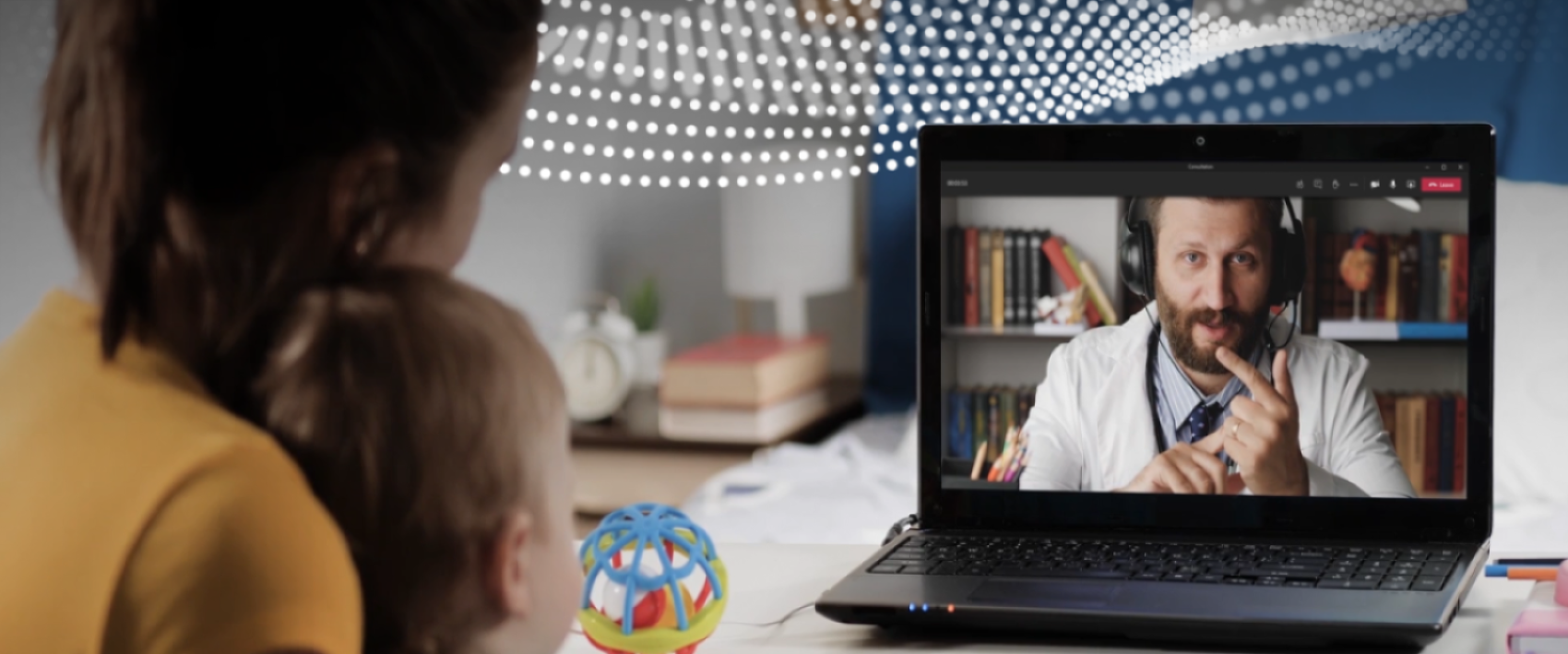 A person holding a child in their lap, looking at the computer which has a doctor on the screen.